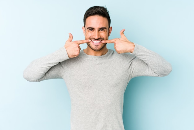 Young caucasian man isolated on blue smiles, pointing fingers at mouth.