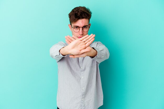 Young caucasian man isolated on blue wall doing a denial gesture