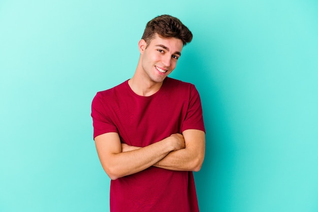 Young caucasian man isolated on blue wall laughing and having fun.