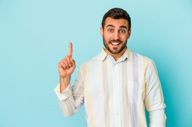 Young caucasian man isolated on blue wall showing number one with finger.