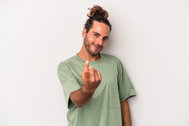 Young caucasian man isolated on gray background pointing with finger at you as if inviting come closer.