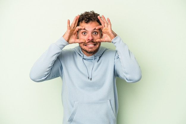 Young caucasian man isolated on green background keeping eyes opened to find a success opportunity.