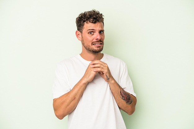 Young caucasian man isolated on green background scared and afraid.