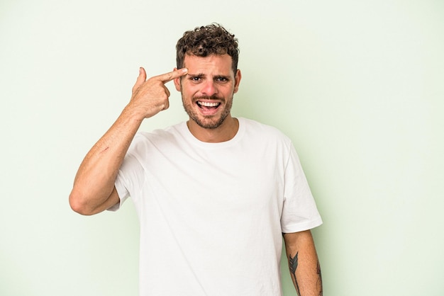 Young caucasian man isolated on green background showing a disappointment gesture with forefinger.