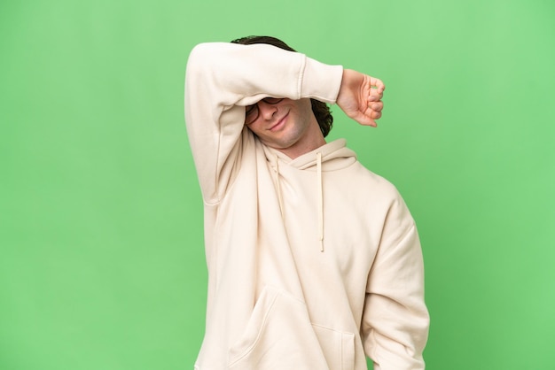 Young caucasian man isolated on green chroma background covering eyes by hands