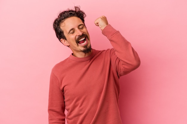 Photo young caucasian man isolated on pink background celebrating a victory, passion and enthusiasm, happy expression.