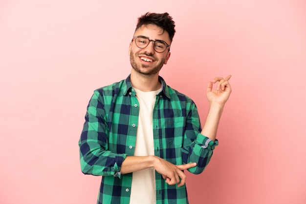 Young caucasian man isolated on pink background happy and pointing up