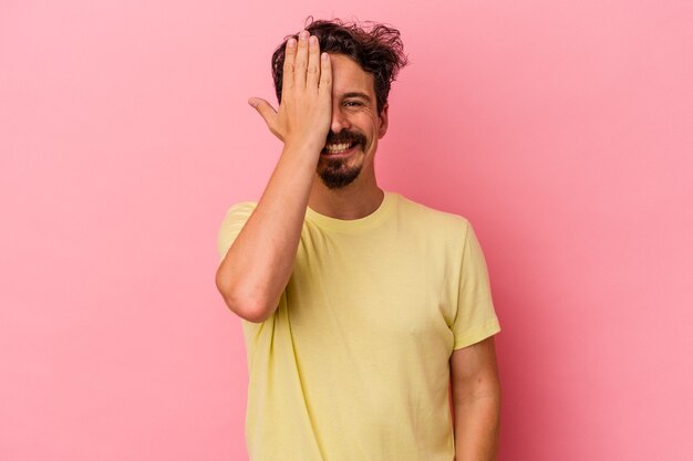 Young caucasian man isolated on pink background having fun covering half of face with palm.