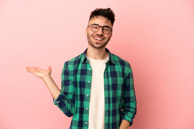 Young caucasian man isolated on pink background holding copyspace imaginary on the palm to insert an ad