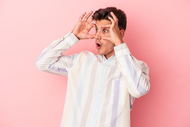 Young caucasian man isolated on pink background keeping eyes opened to find a success opportunity.