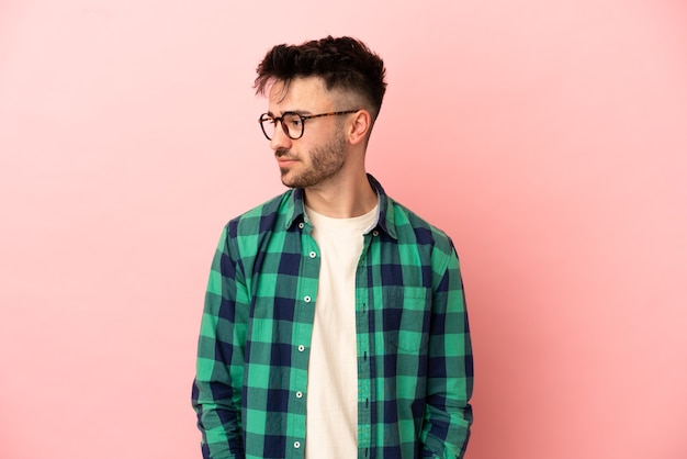 Young caucasian man isolated on pink background looking to the side