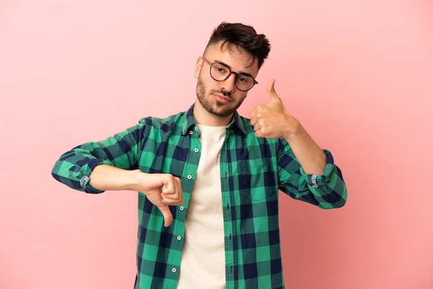 Young caucasian man isolated on pink background making good-bad sign. Undecided between yes or not