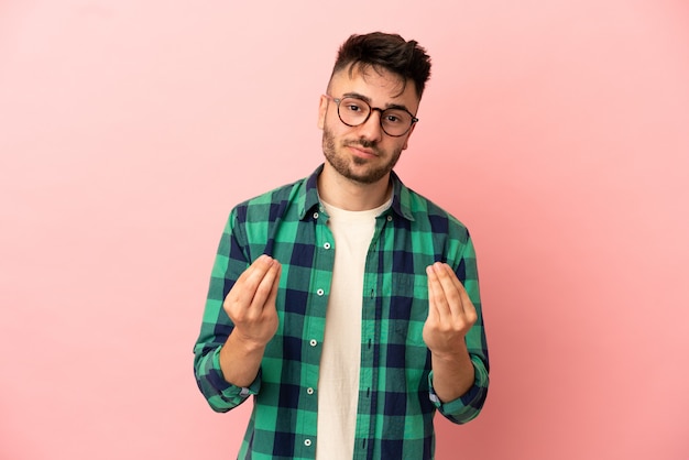 Young caucasian man isolated on pink background making money gesture but is ruined