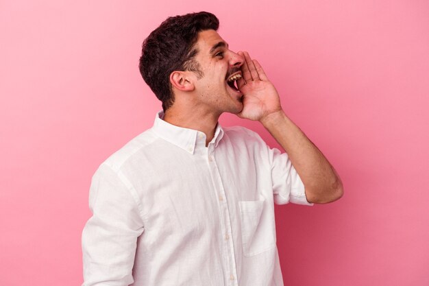 Young caucasian man isolated on pink background shouting and holding palm near opened mouth.