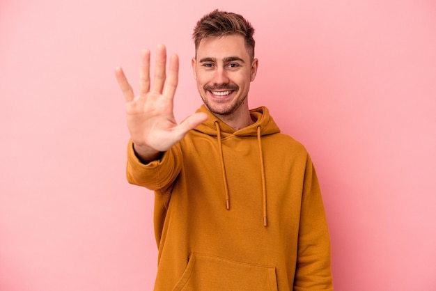 Young caucasian man isolated on pink background smiling cheerful showing number five with fingers.