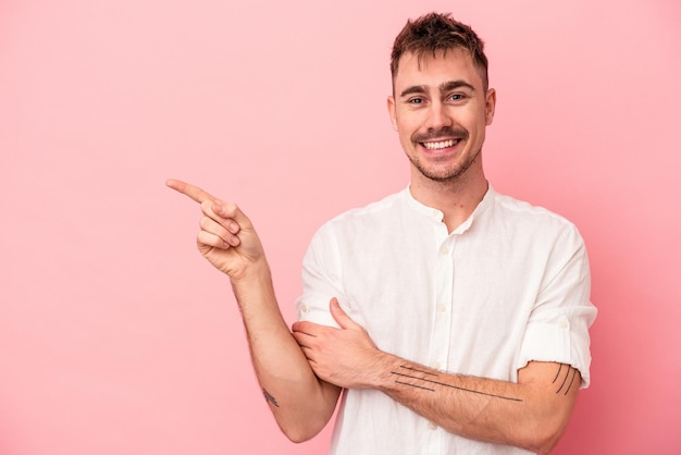 Young caucasian man isolated on pink background smiling cheerfully pointing with forefinger away.