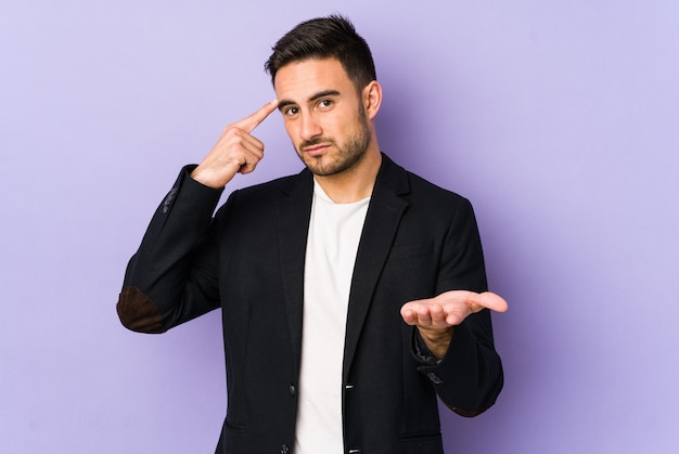 Young caucasian man isolated on purple background holding and showing a product on hand.