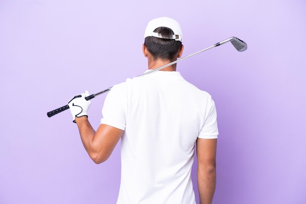 Young caucasian man isolated on purple background playing golf and in back position