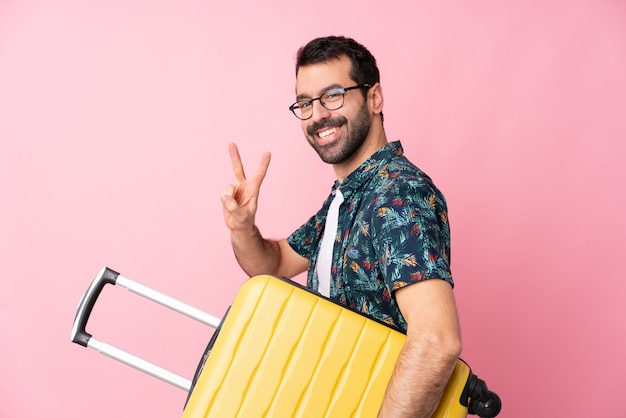 Young caucasian man over isolated wall in vacation with travel suitcase and making victory gesture