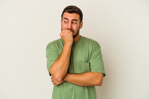 Young caucasian man isolated on white background biting fingernails, nervous and very anxious.