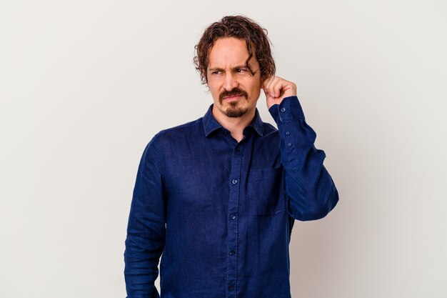 Young caucasian man isolated on white background covering ears with fingers, stressed and desperate by a loudly ambient.