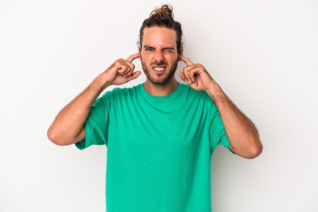 Young caucasian man isolated on white background covering ears with fingers, stressed and desperate by a loudly ambient.