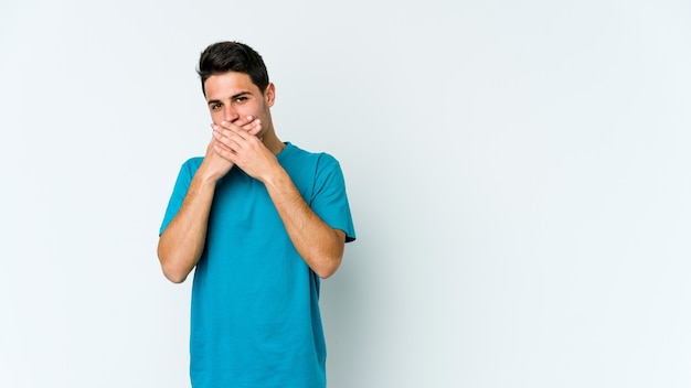 Young caucasian man isolated on white background covering mouth with hands looking worried.