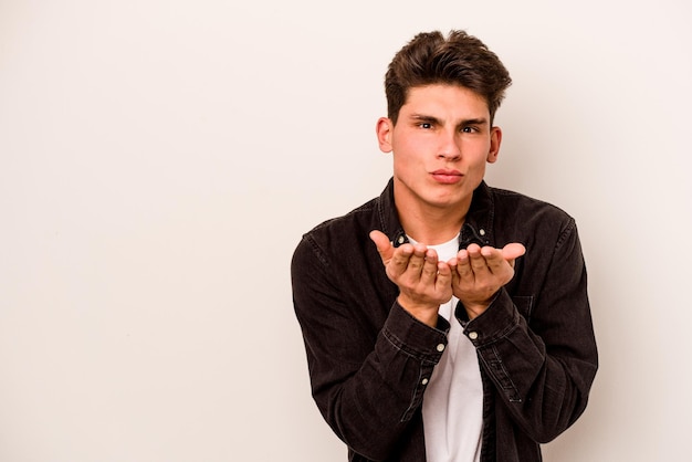 Young caucasian man isolated on white background folding lips and holding palms to send air kiss