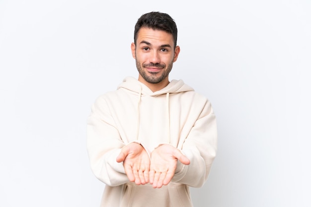 Young caucasian man isolated on white background holding copyspace imaginary on the palm to insert an ad