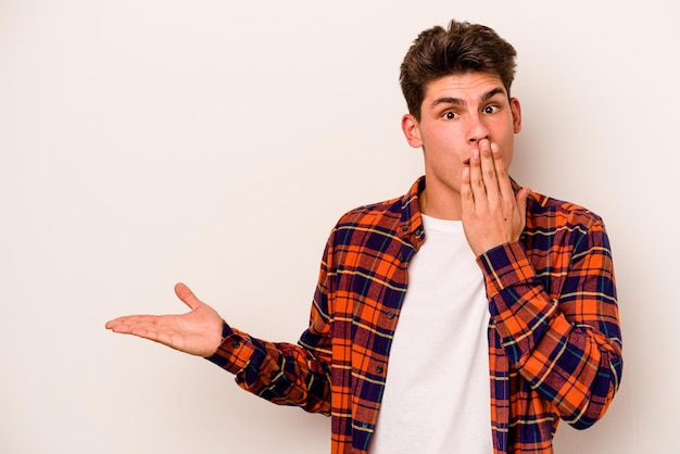 Young caucasian man isolated on white background impressed holding copy space on palm