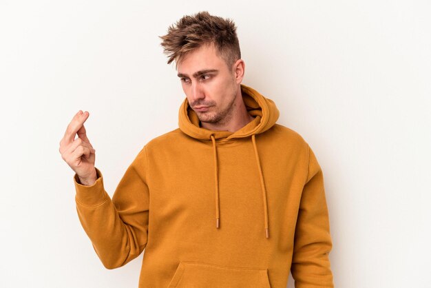 Young caucasian man isolated on white background pointing with finger at you as if inviting come closer.