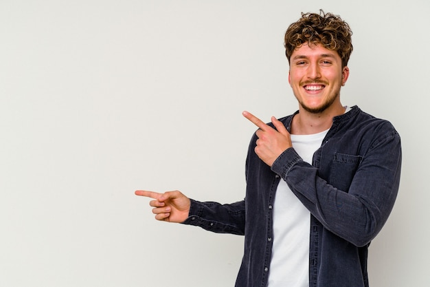 Young caucasian man isolated on white background pointing with forefingers to a copy space, expressing excitement and desire.