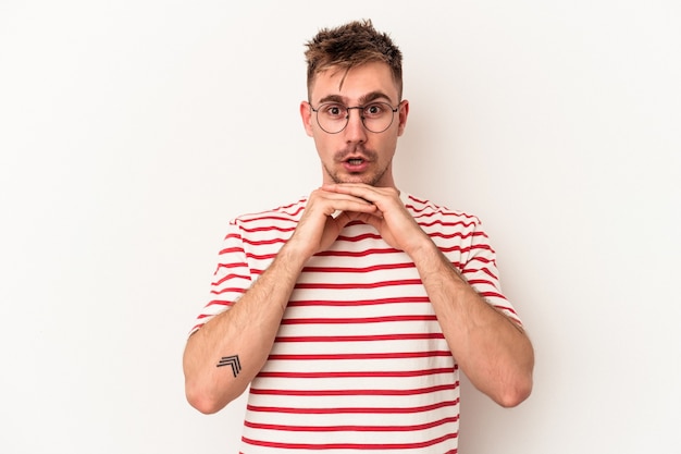 Young caucasian man isolated on white background praying for luck, amazed and opening mouth looking to front.