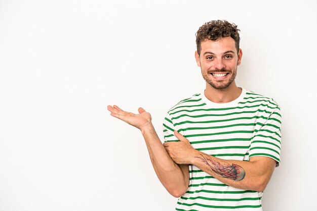 Young caucasian man isolated on white background showing a copy space on a palm and holding another hand on waist.