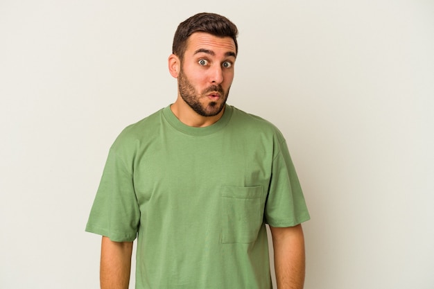 Young caucasian man isolated on white background shrugs shoulders and open eyes confused.