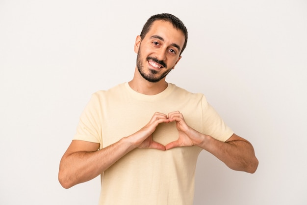 Young caucasian man isolated on white background smiling and showing a heart shape with hands.