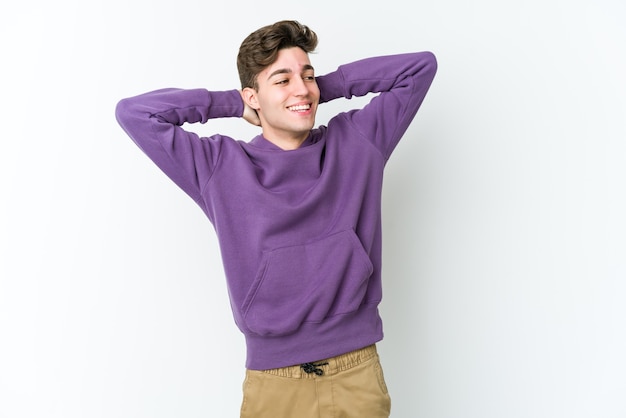 Young caucasian man isolated on white wall feeling confident, with hands behind the head.