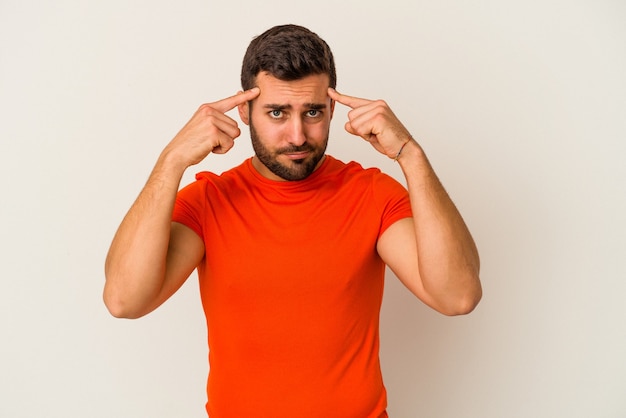 Young caucasian man isolated on white wall focused on a task, keeping forefingers pointing head