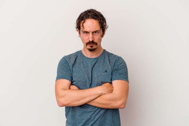 Photo young caucasian man isolated on white wall frowning face in displeasure, keeps arms folded.