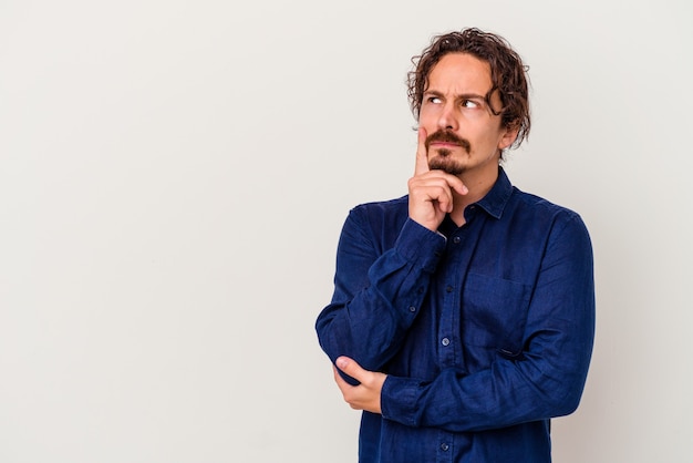 Young caucasian man isolated on white wall looking sideways with doubtful and skeptical expression