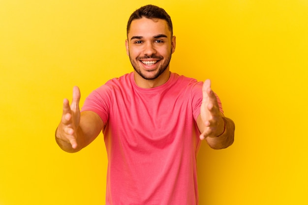 Young caucasian man isolated on yellow background feels confident giving a hug to the camera.