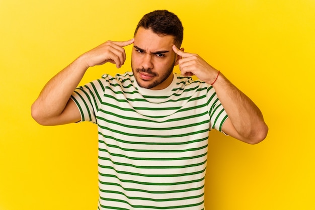 Young caucasian man isolated on yellow background focused on a task, keeping forefingers pointing head.