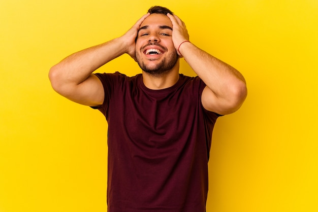 Young caucasian man isolated on yellow background laughs joyfully keeping hands on head. Happiness concept.