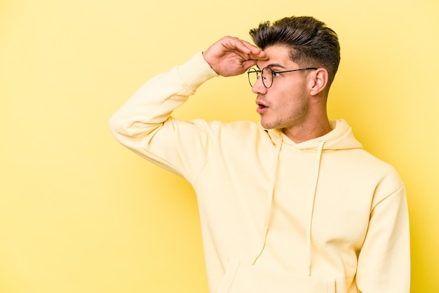 Young caucasian man isolated on yellow background looking far away keeping hand on forehead