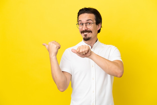 Young caucasian man isolated on yellow background pointing to the side to present a product