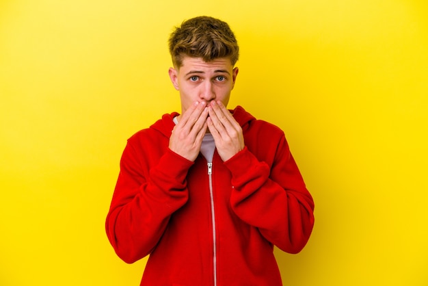 Young caucasian man isolated on yellow background shocked, covering mouth with hands, anxious to discover something new.