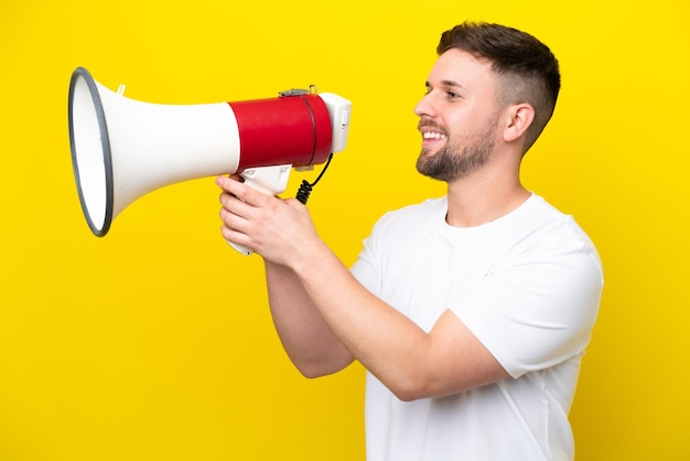 Young caucasian man isolated on yellow background shouting through a megaphone to announce something