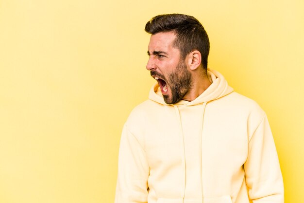 Young caucasian man isolated on yellow background shouting very angry rage concept frustrated