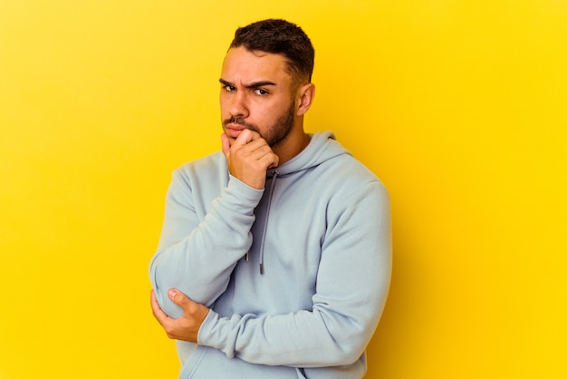 Young caucasian man isolated on yellow background suspicious, uncertain, examining you.