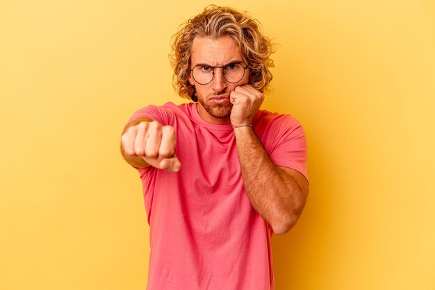 Photo young caucasian man isolated on yellow background throwing a punch, anger, fighting due to an argument, boxing.